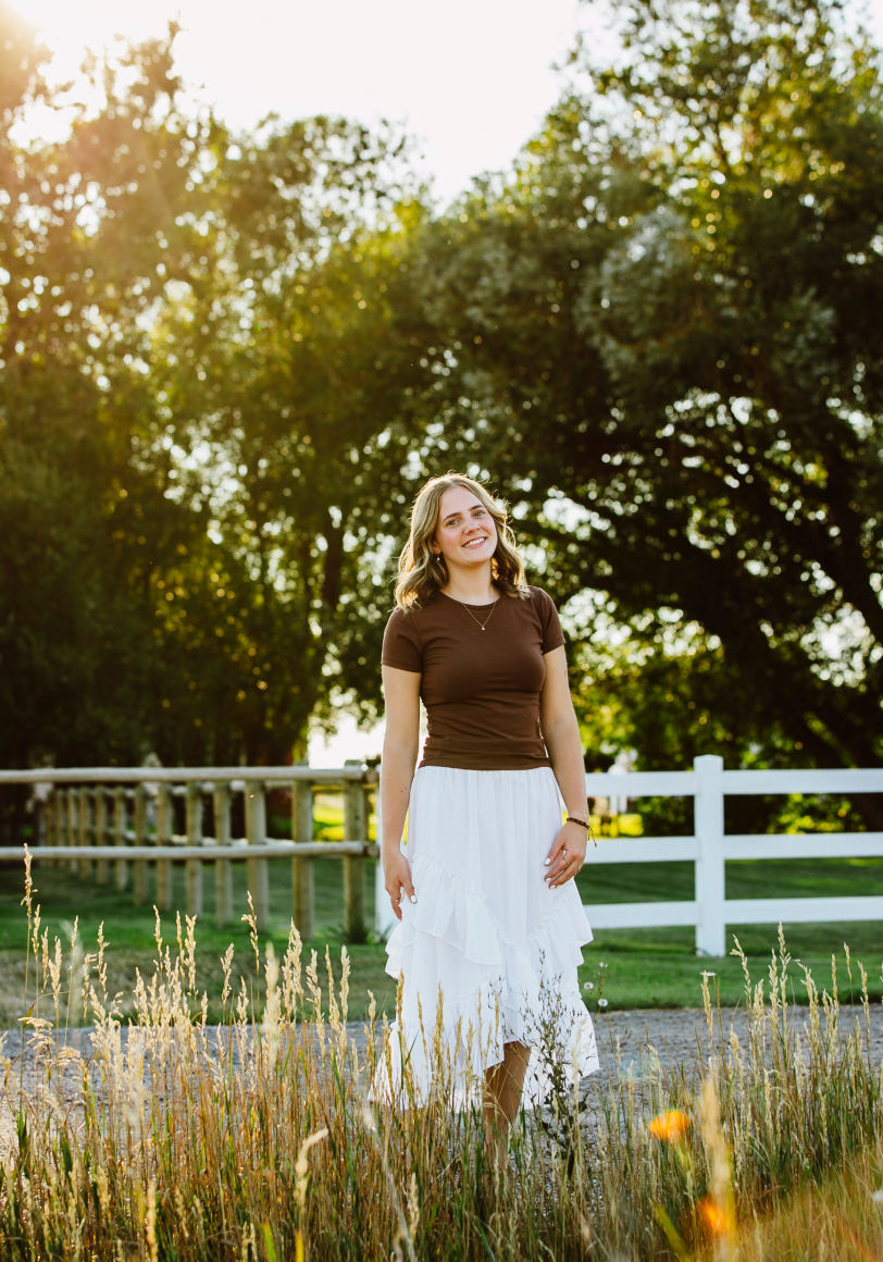 The artist standing in a sunlit grassy field by a white fence